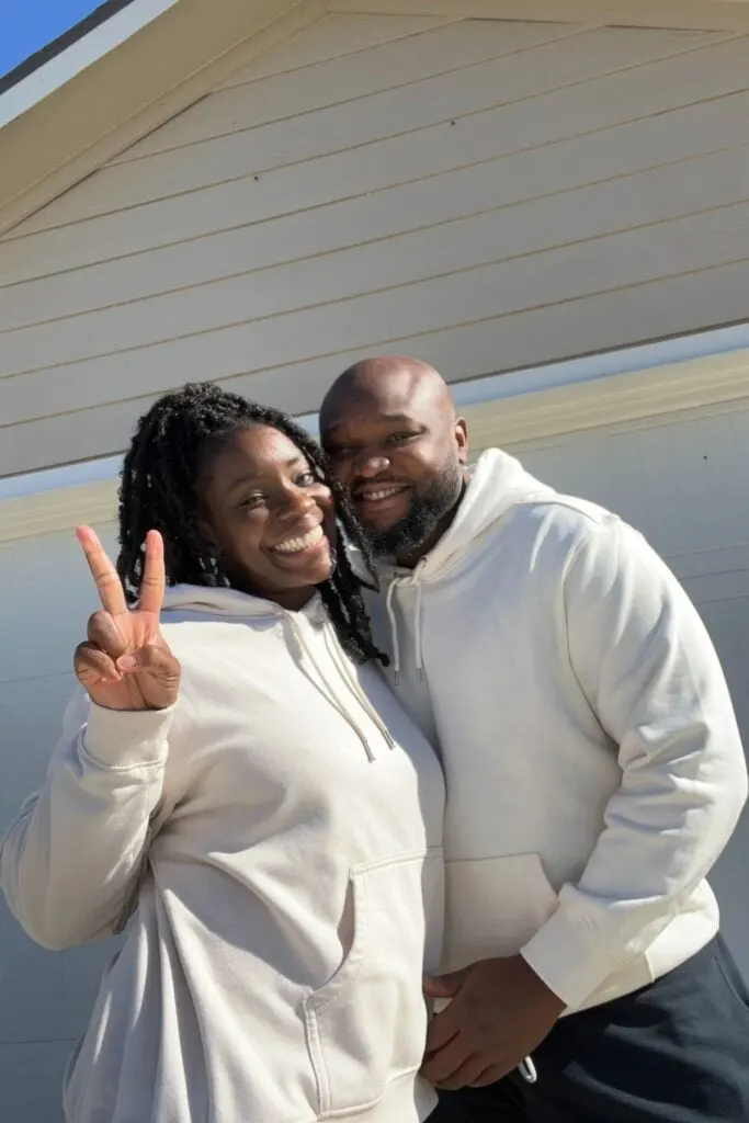 black couple in matching sweatshirt laughing into the camera in front of a garage entrance