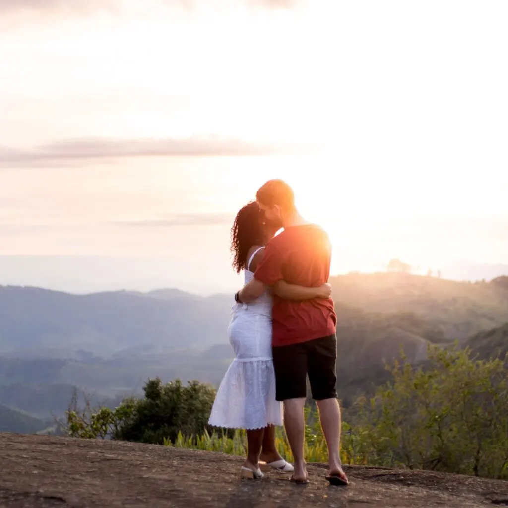 young couple standing on a hill watching the sunset and hugging