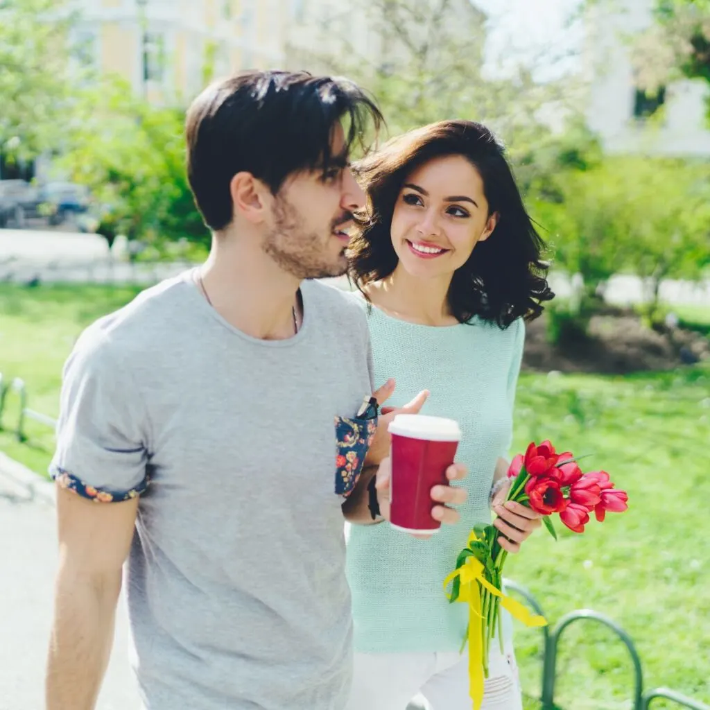 young couple walking through the park with flowers