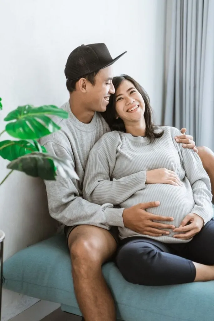 young couple sitting on the couch laughing and stroking the pregnant belly