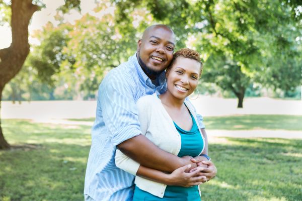 black couple smiling into the camera with a park in the background